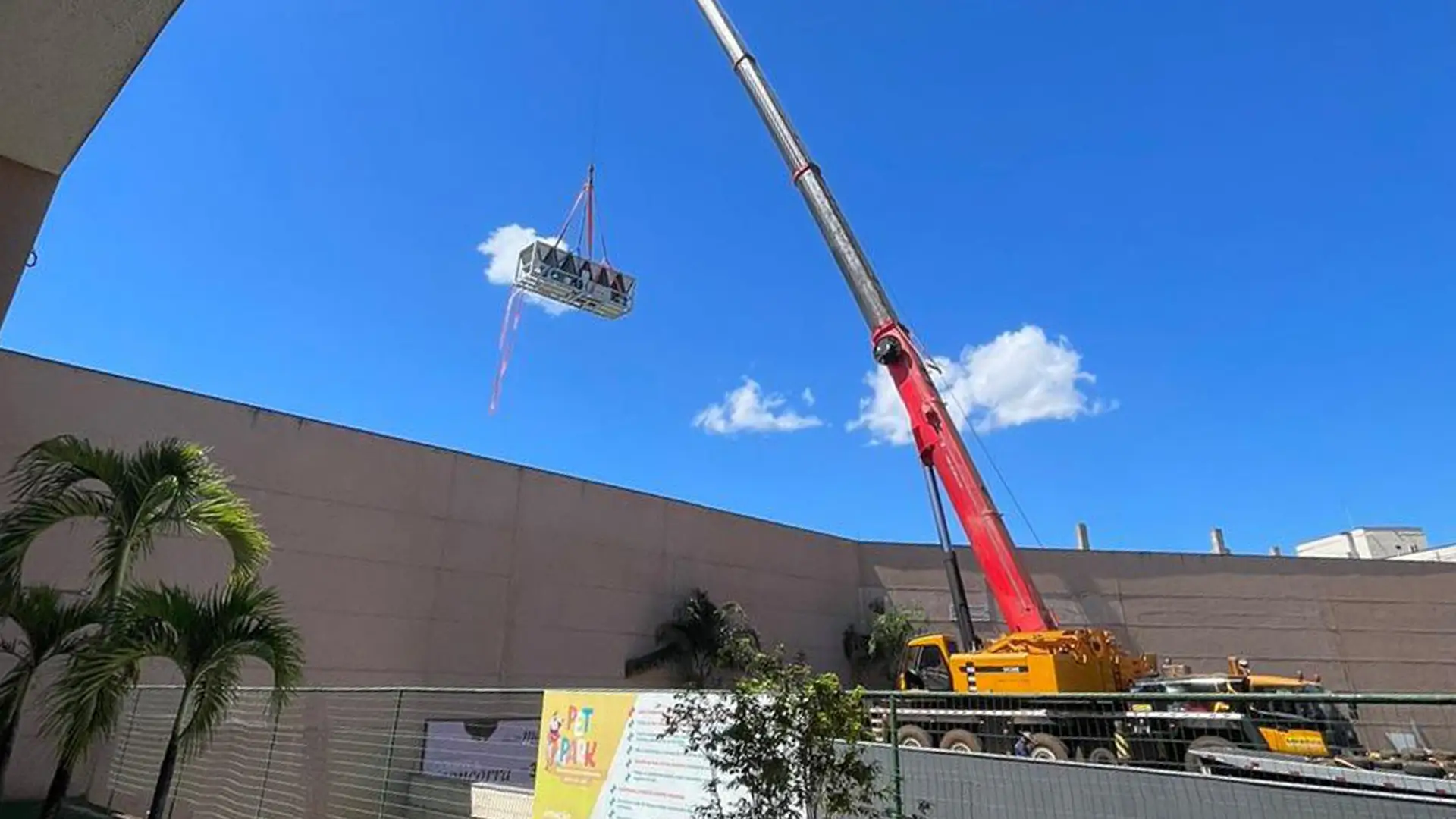 Guindaste içando chiller em área externa sob céu azul.