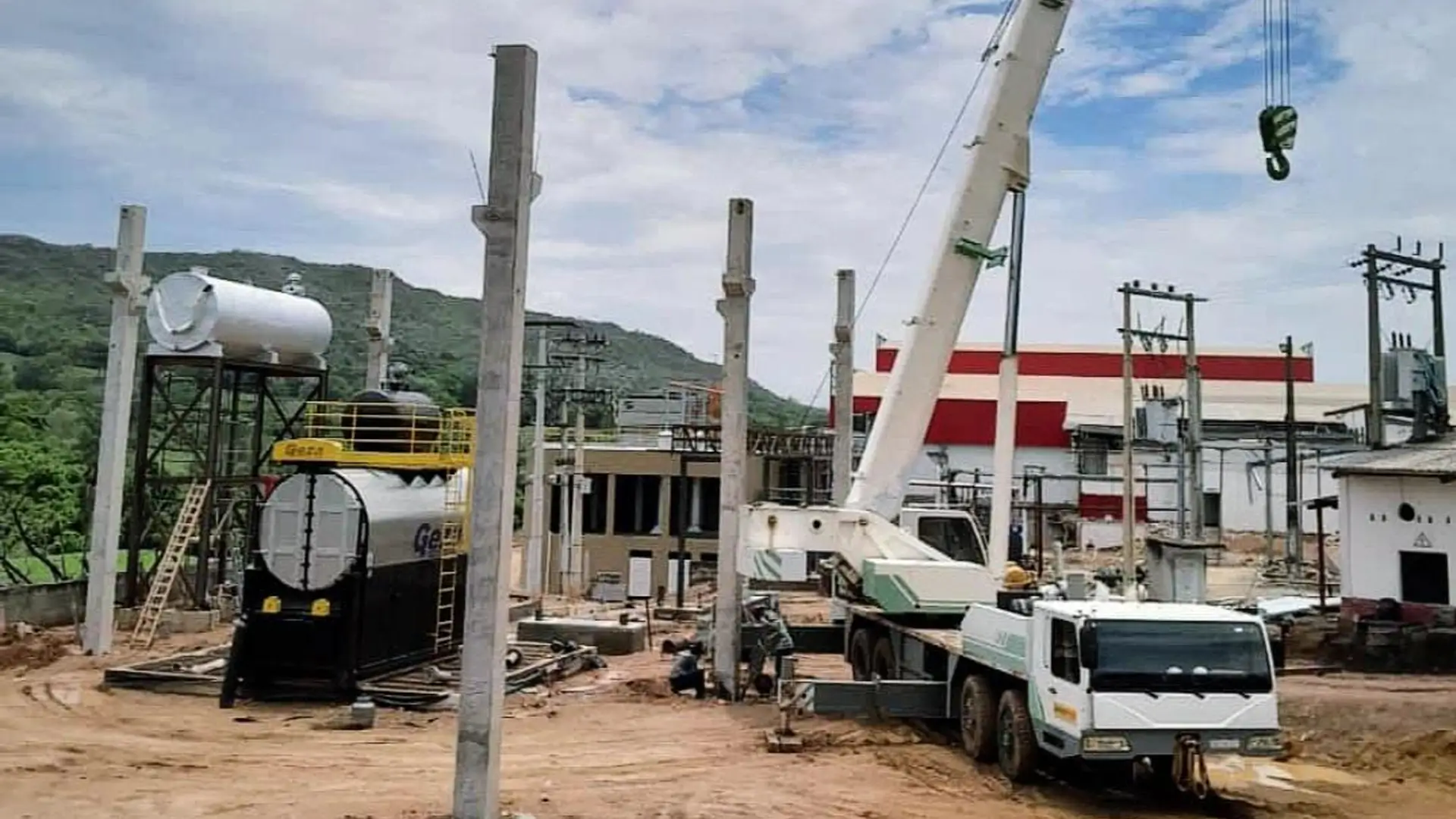Caminhão guindaste branco realizando o içamento e montagem de pilares de concreto pré-moldado em um canteiro de obras industrial