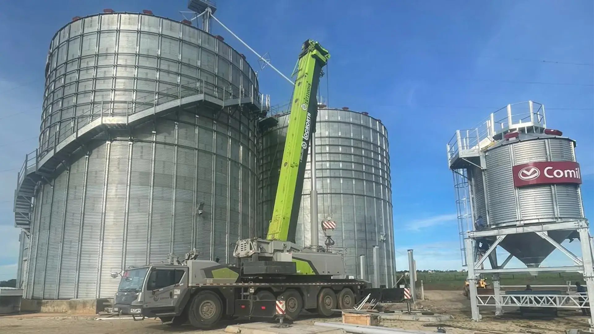 Caminhão guindaste realizando o içamento de estruturas metálicas para a montagem de infraestrutura agrícola no agronegócio.
